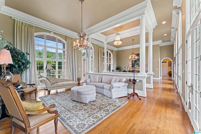 living room featuring light hardwood / wood-style floors, ornate columns, an inviting chandelier, and crown molding