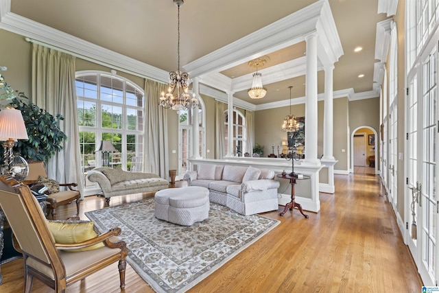 living room featuring an inviting chandelier, ornate columns, ornamental molding, french doors, and light wood-type flooring