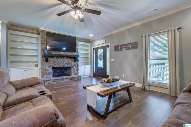 living room with crown molding, a stone fireplace, dark hardwood / wood-style flooring, and built in features