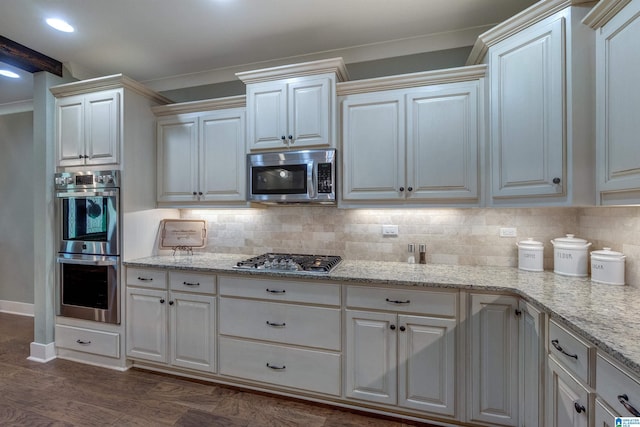 kitchen with dark wood-type flooring, appliances with stainless steel finishes, backsplash, light stone countertops, and ornamental molding