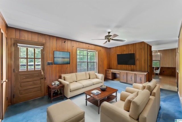 carpeted living room with a wealth of natural light, ceiling fan, and wood walls