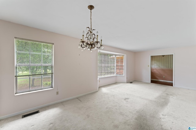 carpeted empty room with an inviting chandelier