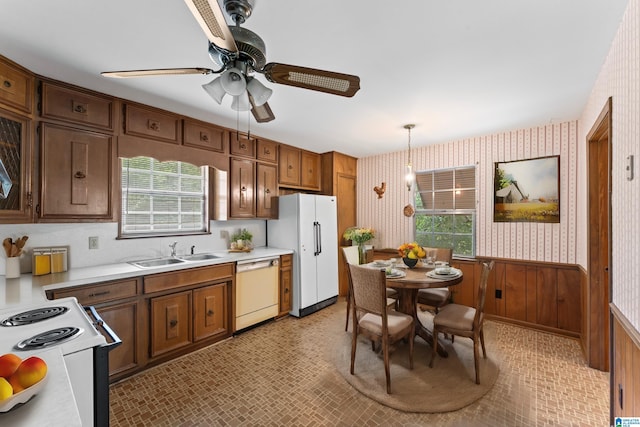 kitchen with wooden walls, sink, hanging light fixtures, a healthy amount of sunlight, and white appliances