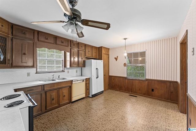 kitchen featuring pendant lighting, wooden walls, sink, plenty of natural light, and white appliances