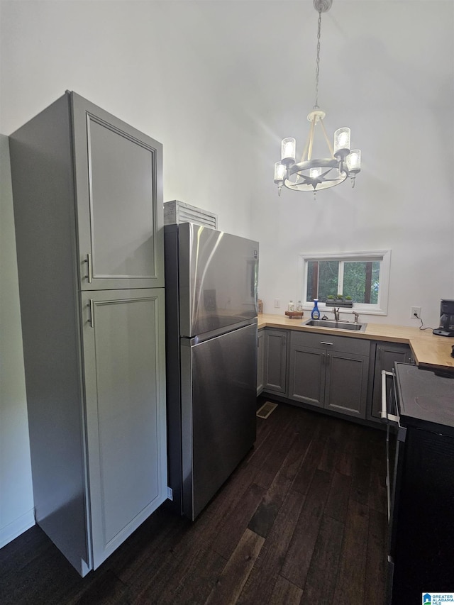 kitchen with gray cabinets, stainless steel refrigerator, a towering ceiling, dark hardwood / wood-style floors, and decorative light fixtures