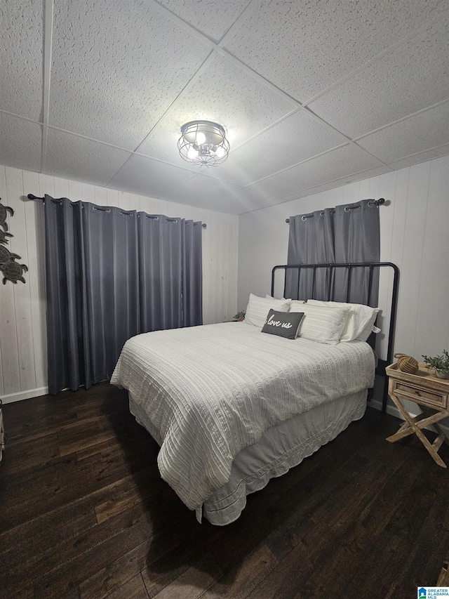 bedroom with dark wood-type flooring, wooden walls, and a drop ceiling