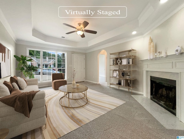 living room with a premium fireplace, ceiling fan, light colored carpet, a tray ceiling, and crown molding