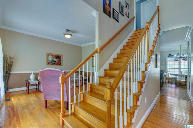 staircase with an inviting chandelier, wood-type flooring, and ornamental molding