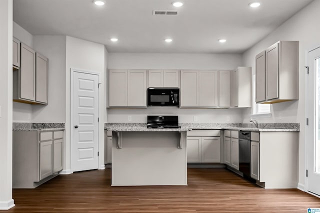 kitchen with gray cabinets, light stone counters, black appliances, a kitchen island, and dark hardwood / wood-style flooring