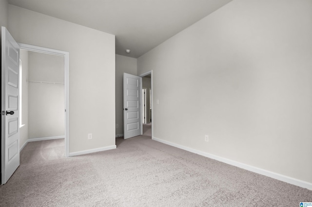 unfurnished bedroom featuring a walk in closet, light colored carpet, and a closet