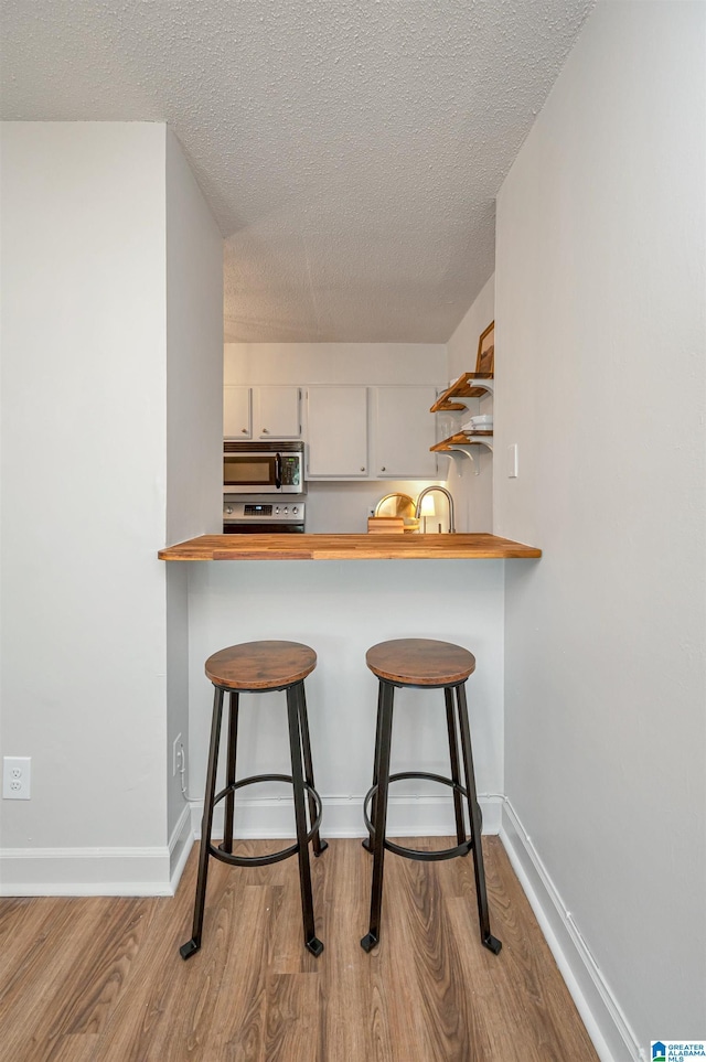 kitchen with light hardwood / wood-style floors, appliances with stainless steel finishes, white cabinetry, and a breakfast bar area