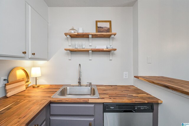 kitchen with sink, butcher block counters, dishwasher, a textured ceiling, and white cabinets