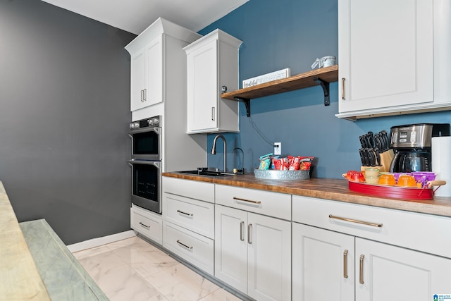 kitchen with white cabinetry, stainless steel double oven, and sink