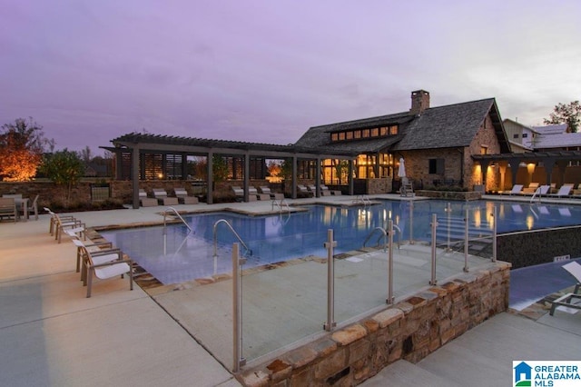 pool at dusk featuring a pergola and a patio