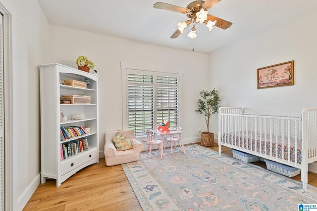 bedroom with light hardwood / wood-style floors, a nursery area, and ceiling fan