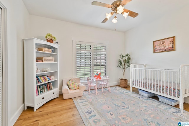 bedroom featuring ceiling fan, light hardwood / wood-style floors, and a crib