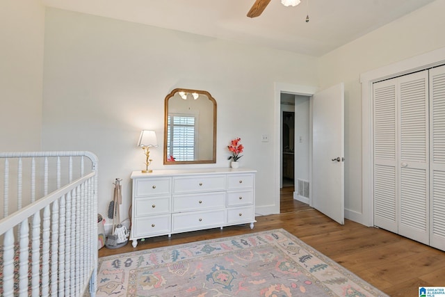 bedroom with hardwood / wood-style flooring, a crib, a closet, and ceiling fan