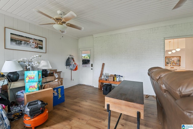 living room featuring wood-type flooring, ornamental molding, ceiling fan, and brick wall