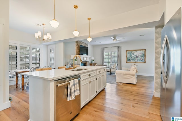 kitchen featuring appliances with stainless steel finishes, an island with sink, pendant lighting, a fireplace, and white cabinets