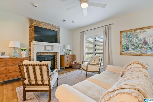 living room with ceiling fan, a fireplace, and light wood-type flooring