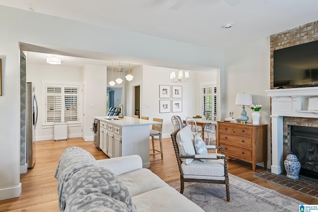 living room featuring sink, a fireplace, a chandelier, and light wood-type flooring