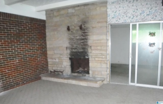 unfurnished living room featuring brick wall, a stone fireplace, carpet, and beam ceiling