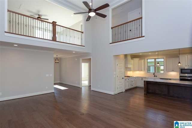 unfurnished living room featuring ceiling fan, dark hardwood / wood-style floors, sink, and a high ceiling