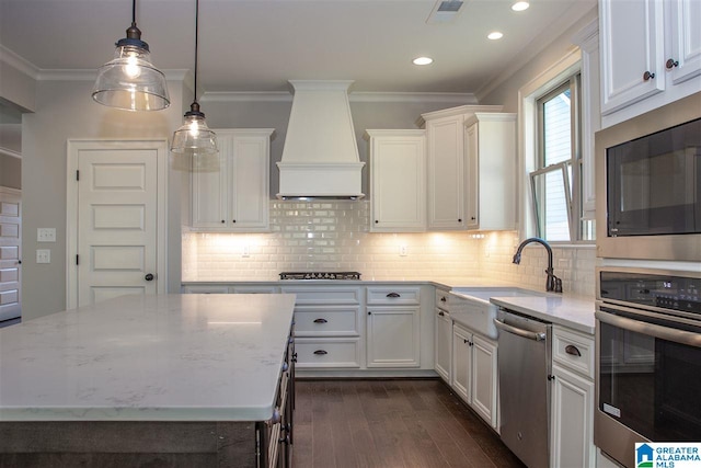 kitchen with appliances with stainless steel finishes, white cabinetry, sink, custom exhaust hood, and a center island