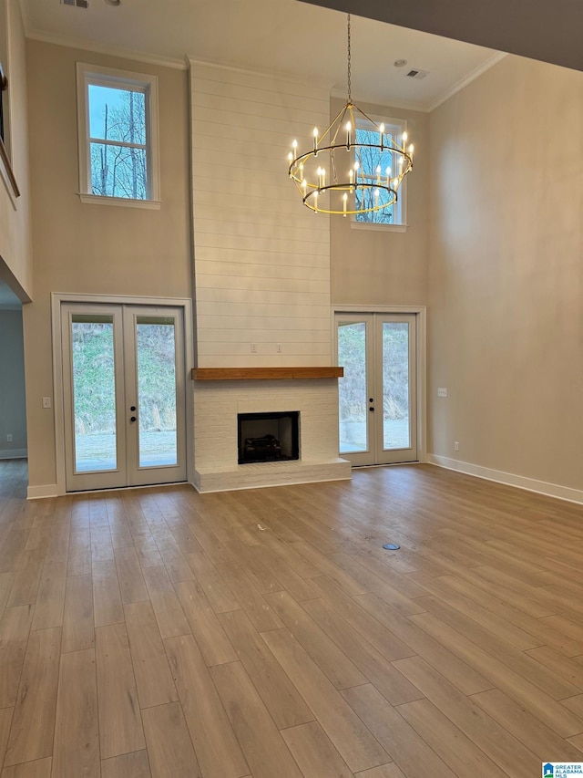 unfurnished living room featuring french doors, a large fireplace, an inviting chandelier, and light wood-type flooring