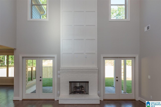 unfurnished living room with french doors, a towering ceiling, a fireplace, and dark hardwood / wood-style flooring