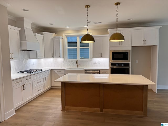 kitchen featuring white cabinetry, appliances with stainless steel finishes, a kitchen island, custom range hood, and pendant lighting