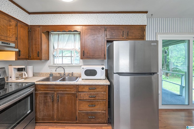 kitchen with ventilation hood, appliances with stainless steel finishes, sink, and light hardwood / wood-style floors