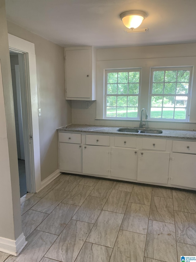 kitchen with visible vents, a sink, tasteful backsplash, white cabinetry, and baseboards