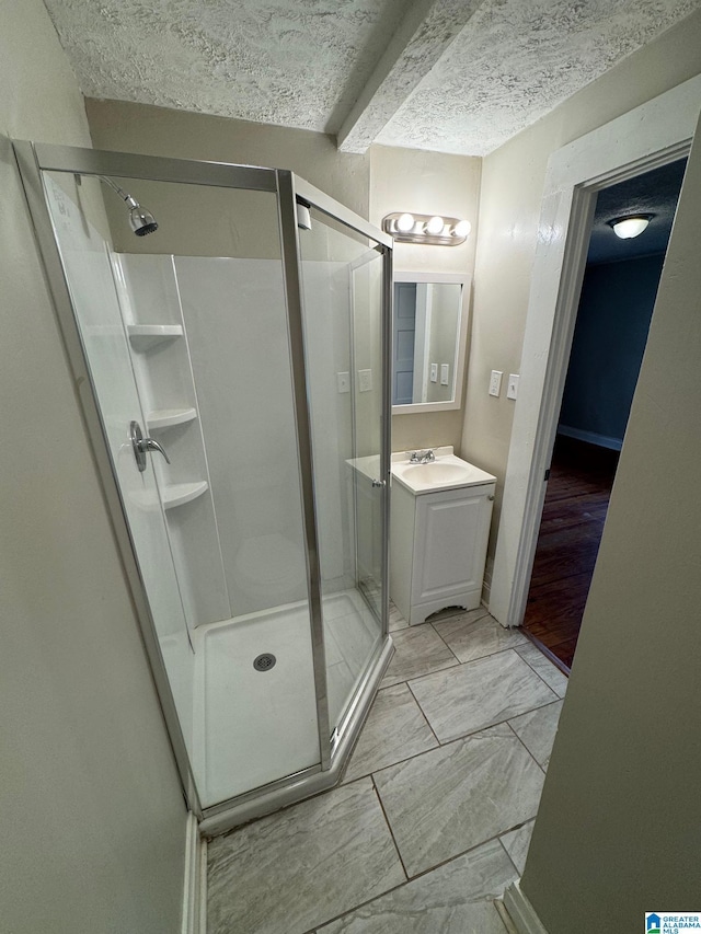 bathroom with beamed ceiling, vanity, a shower with door, and a textured ceiling