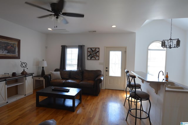 living room featuring ceiling fan with notable chandelier, sink, and light wood-type flooring