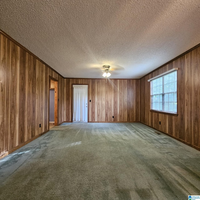 empty room featuring light carpet, wooden walls, and a textured ceiling