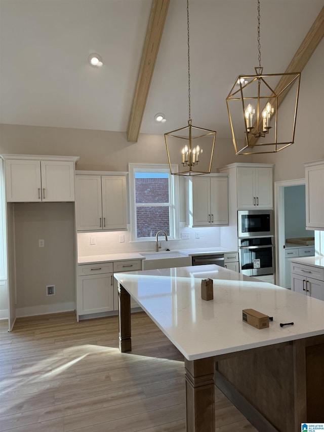 kitchen featuring built in microwave, sink, white cabinetry, stainless steel oven, and hanging light fixtures