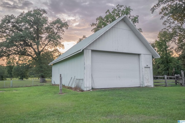 garage at dusk featuring a lawn