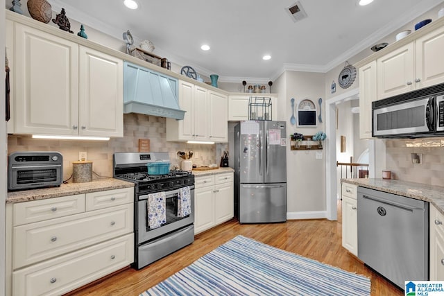 kitchen with appliances with stainless steel finishes, light hardwood / wood-style flooring, premium range hood, and tasteful backsplash