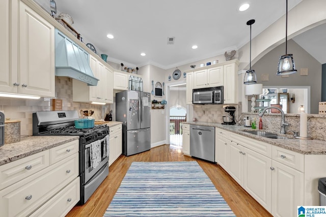 kitchen with appliances with stainless steel finishes, backsplash, custom exhaust hood, light hardwood / wood-style flooring, and sink