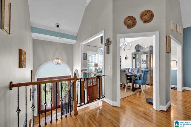 hall with high vaulted ceiling, a chandelier, and light hardwood / wood-style floors