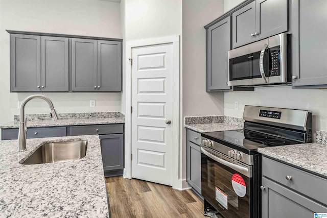 kitchen with wood-type flooring, sink, gray cabinetry, stainless steel appliances, and light stone countertops