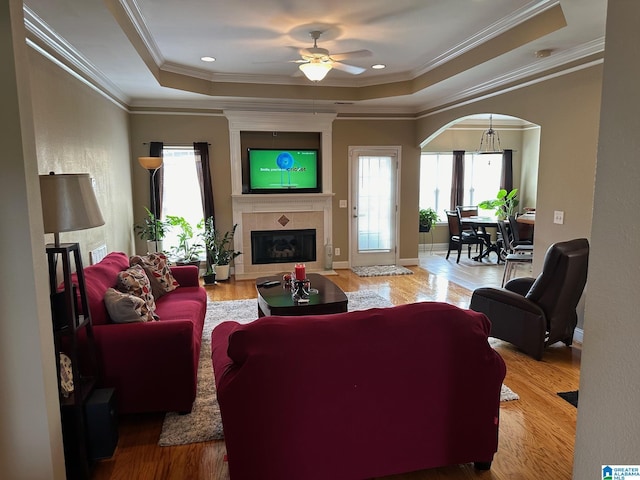 living room with crown molding, wood-type flooring, a tray ceiling, ceiling fan, and a fireplace