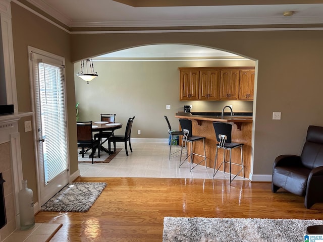 interior space with a breakfast bar, decorative light fixtures, sink, crown molding, and light hardwood / wood-style flooring