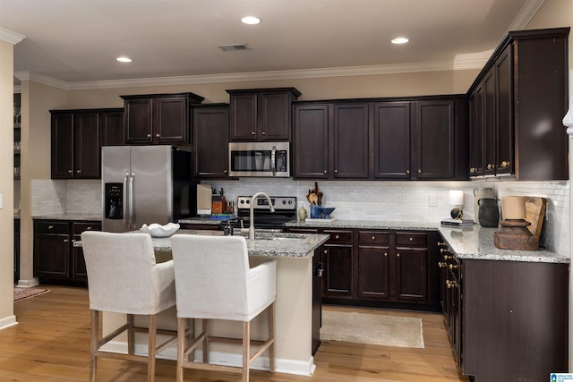 kitchen with a breakfast bar, stainless steel appliances, light stone countertops, a center island with sink, and light wood-type flooring