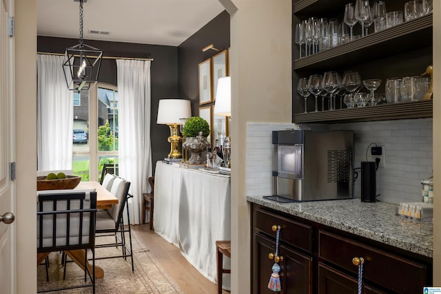 bar with pendant lighting, tasteful backsplash, light stone countertops, dark brown cabinets, and light hardwood / wood-style flooring