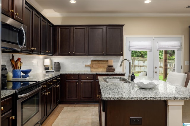 kitchen with sink, stainless steel appliances, a center island with sink, decorative backsplash, and light wood-type flooring