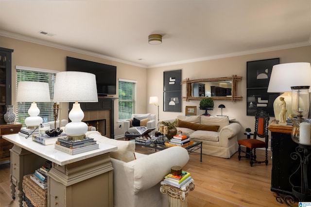 living room featuring a tile fireplace, ornamental molding, and light wood-type flooring