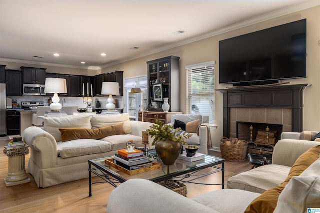 living room featuring a tiled fireplace, crown molding, and light hardwood / wood-style floors