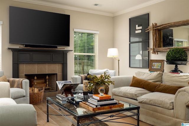 living room with a tiled fireplace, ornamental molding, and light wood-type flooring